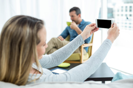 Pregnant woman sitting on sofa and using smartphone
