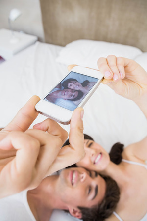 Couple lying on bed and taking a selfie on mobile phoneの写真素材