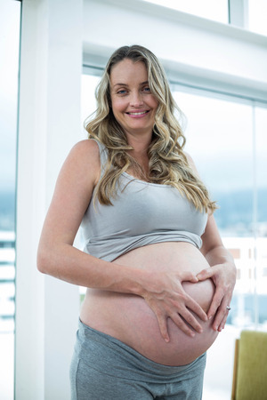 Portrait of pregnant woman holding her stomach in bedroomの写真素材