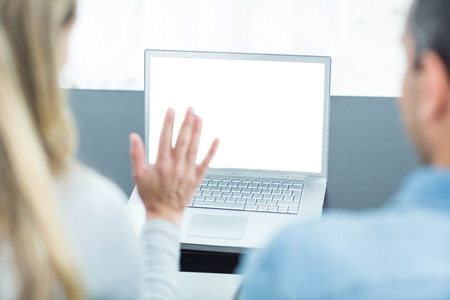 Couple sitting on sofa and using laptop in living roomの写真素材