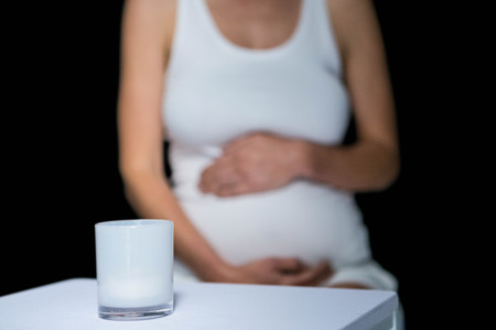 Pregnant woman touching belly, glass on table on black backgroundの写真素材