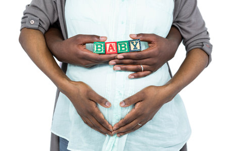 Pregnant woman with baby cubes on her belly and husband hugging from behind on white backgroundのeditorial素材