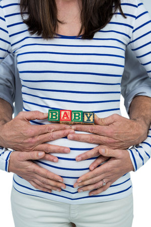 Pregnant woman with baby cubes on her belly and husband hugging from behind on white backgroundのeditorial素材