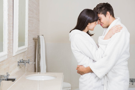 Young couple in bathrobe standing face to face at home in the bathroomの写真素材