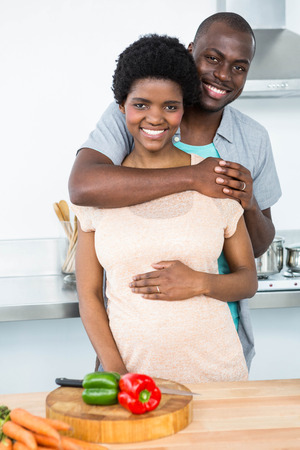 Portrait of pregnant couple embracing each other in kitchen at homeの写真素材