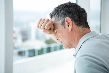 Tensed man leaning on glass window at homeの写真素材