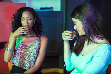 Two women having tequila at nightclubの写真素材