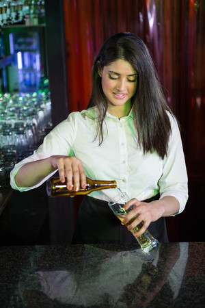 Pretty bartender preparing a drink at bar counter in barの写真素材