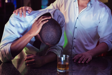 Man comforting his depressed friend in bar