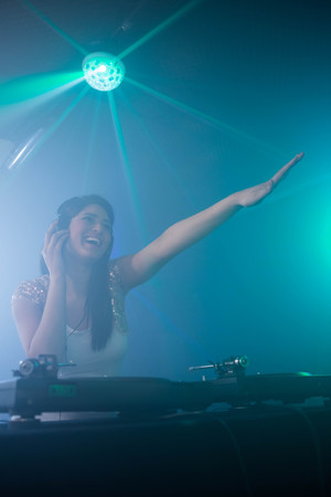 Pretty female DJ waving her hand while playing music at nightclub