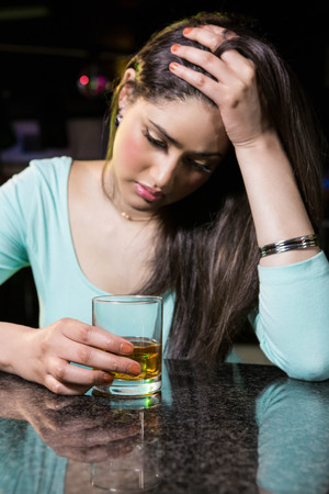 Depressed woman having whiskey at bar counter in barの写真素材