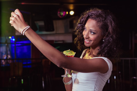 Young women taking a selfie while having a cocktail drink in barの写真素材