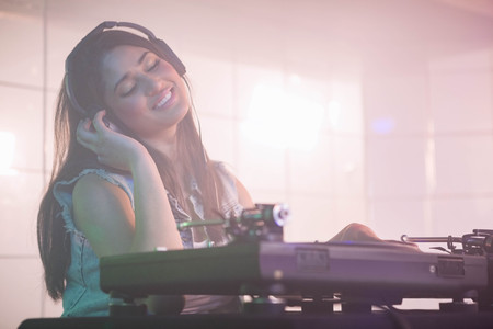 Pretty female DJ listening to the headphone while playing music at nightclubの写真素材