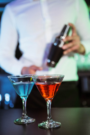 Two glasses of cocktail on bar counter and bartender holding shaker in backgroundの写真素材