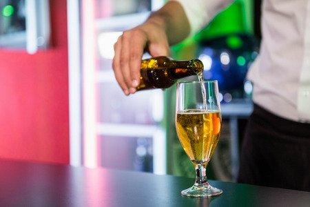 Mid section of bartender pouring beer in a glass at bar counterの写真素材