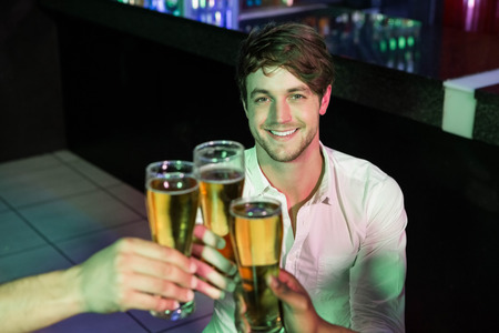 Happy man toasting his glass of beer with friends in barの写真素材