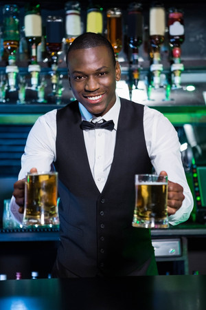 Bartender serving two glasses of beer at bar counter in barの写真素材