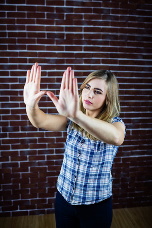 Pretty blonde woman looking through her hands on brick wall backgroundの写真素材