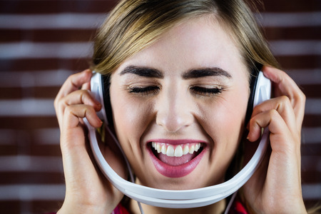 Pretty blonde woman listening to music on brick wall backgroundの写真素材