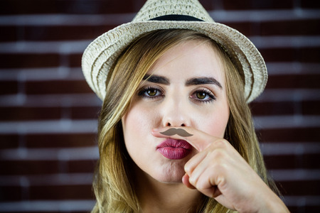 Pretty blonde woman doing a moustache with her finger on brick wall backgroundの写真素材