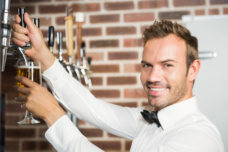 Handsome barman pouring a pint of beer in a pubの写真素材