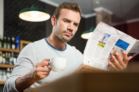 Handsome man reading newspaper and having a coffee in a pubの写真素材