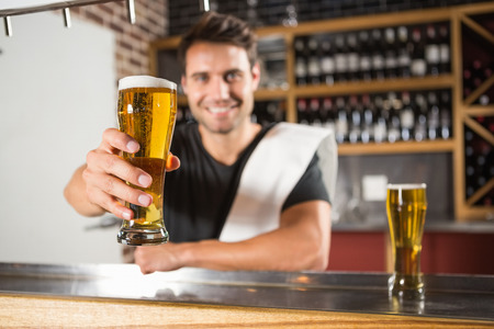 Handsome barman holding a pint of beer in a pubの写真素材