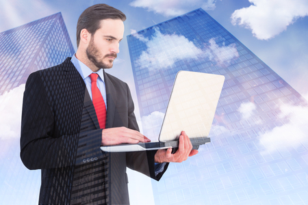 Focused businessman using his laptop against low angle view of skyscrapersの写真素材