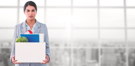 Fired businesswoman holding box of belongings against view of a cityの写真素材
