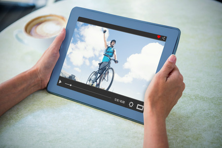 Fit man cycling on rocky terrain and cheering against person holding tablet computer at table in...