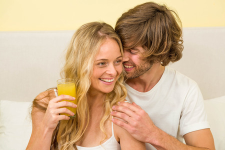 Cute couple having breakfast sitting on their bed in the bedroomの写真素材