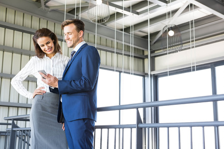 Businessman and businesswoman looking at smartphone in officeの写真素材