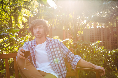 Man sitting on a bench with a glass of red wine in the gardenの写真素材