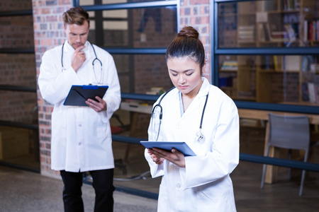 Female doctor using digital tablet near library and male doctor standing behind and thinking