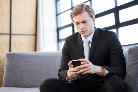 Businessman text messaging on mobile phone in officeの写真素材