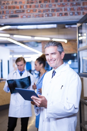 Portrait of male doctor using digital tablet in hospital and colleagues standing behind and discussingの写真素材