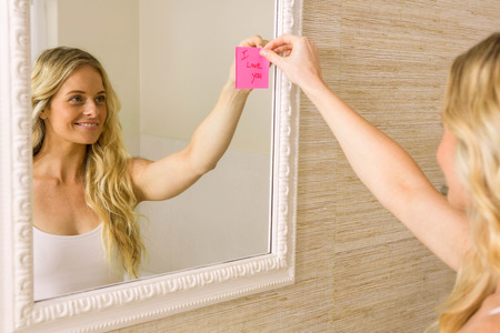 Beautiful blonde putting I love you note on mirror in the bathroomの写真素材