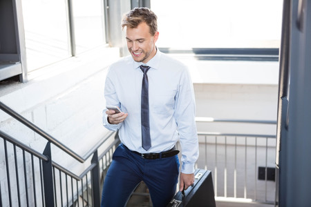 Businessman using phone and climbing staircase in officeの写真素材