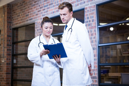 Two doctors looking at clipboard and discussing near library in hospital