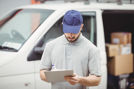 Delivery man writing on clipboard in front of his vanの写真素材