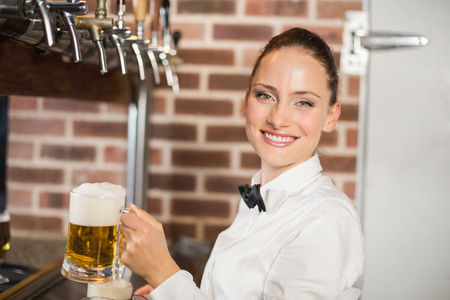 Attractive barmaid holding beers while smiling at camera in a barの写真素材