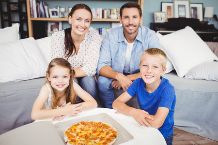 Portrait of smiling family with pizza on table at homeの写真素材