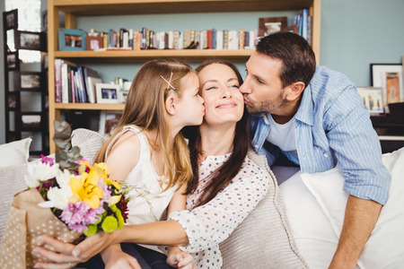 Father and daughter kissing mother at homeの写真素材