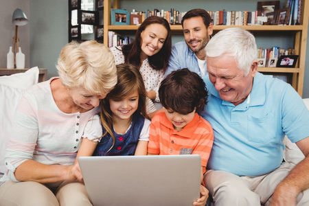 Smiling children and grandparents using laptop with family at homeの写真素材