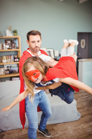 Father carrying daughter wearing superhero costume at homeの写真素材