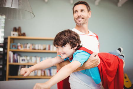 Father carrying son with superhero costume at homeの写真素材
