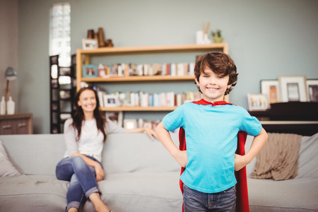 Portrait of smiling boy wearing superhero costume with mother sitting on sofa at homeの写真素材