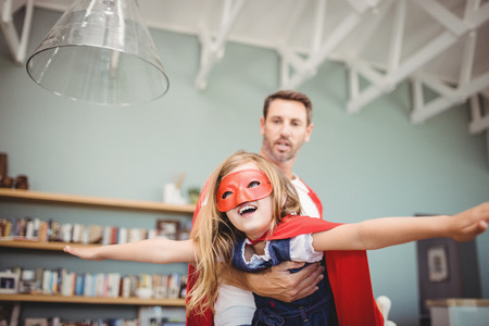 Father carrying daughter with superhero costume at homeの写真素材
