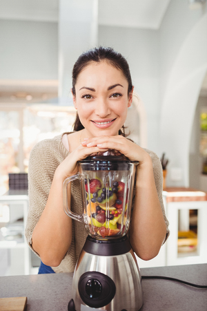 Portrait of cheerful woman preparing fruit juice at homeの写真素材