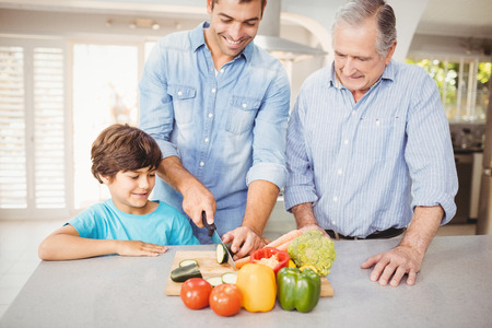 Man chopping vegetable with son and father at kitchen tableの写真素材